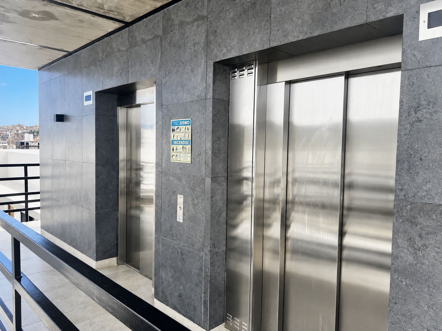 Een moderne lift met een metalen afwerking, een veiligheidssign en een helder uitzicht op de skyline.