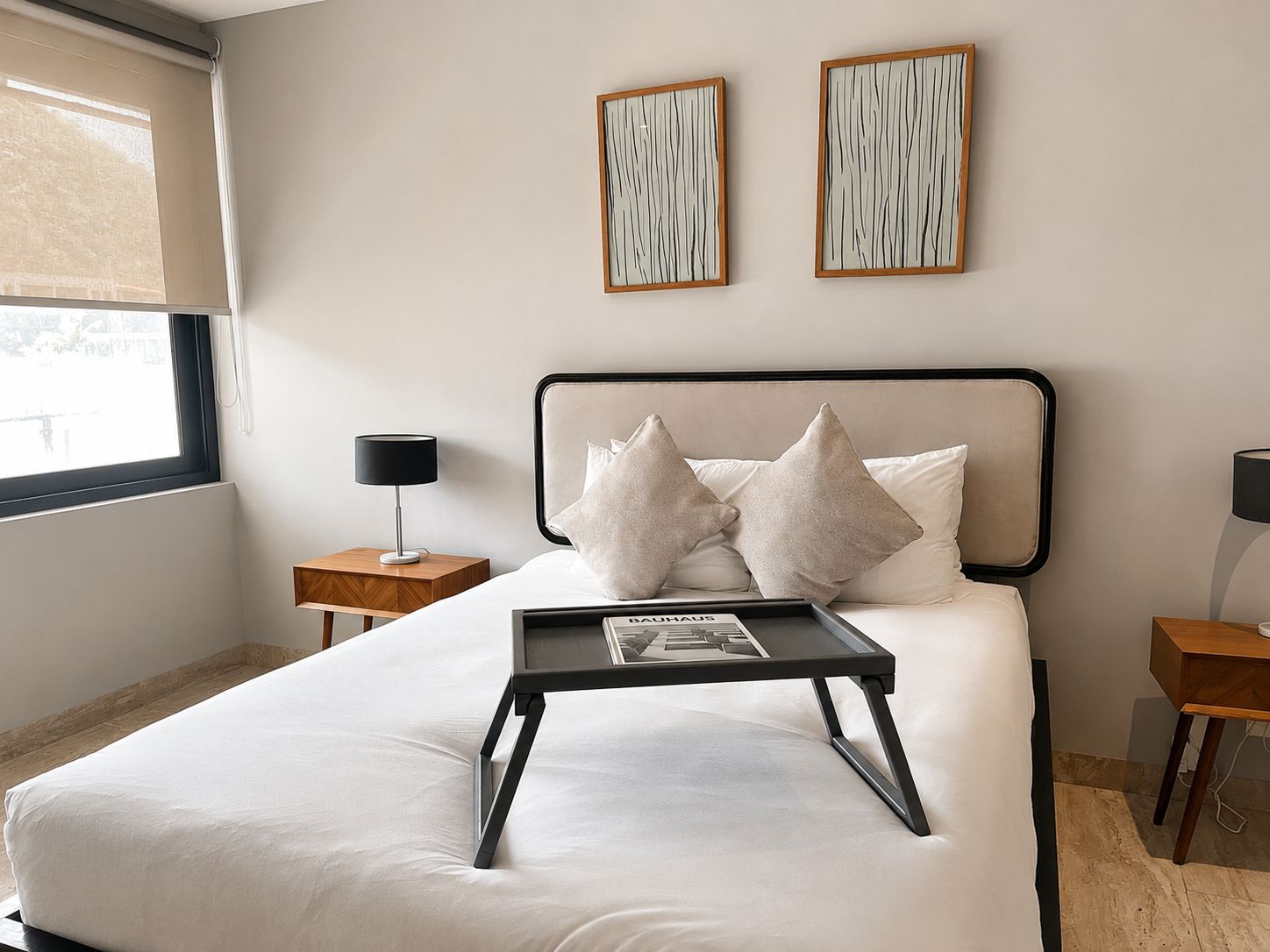 Une chambre à coucher avec un lit, des tables de chevet, une fenêtre et des œuvres d’art accrochées au mur.