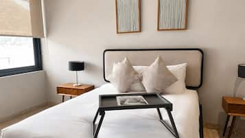 Une chambre à coucher avec un lit, des tables de chevet, une fenêtre et des œuvres d’art accrochées au mur.