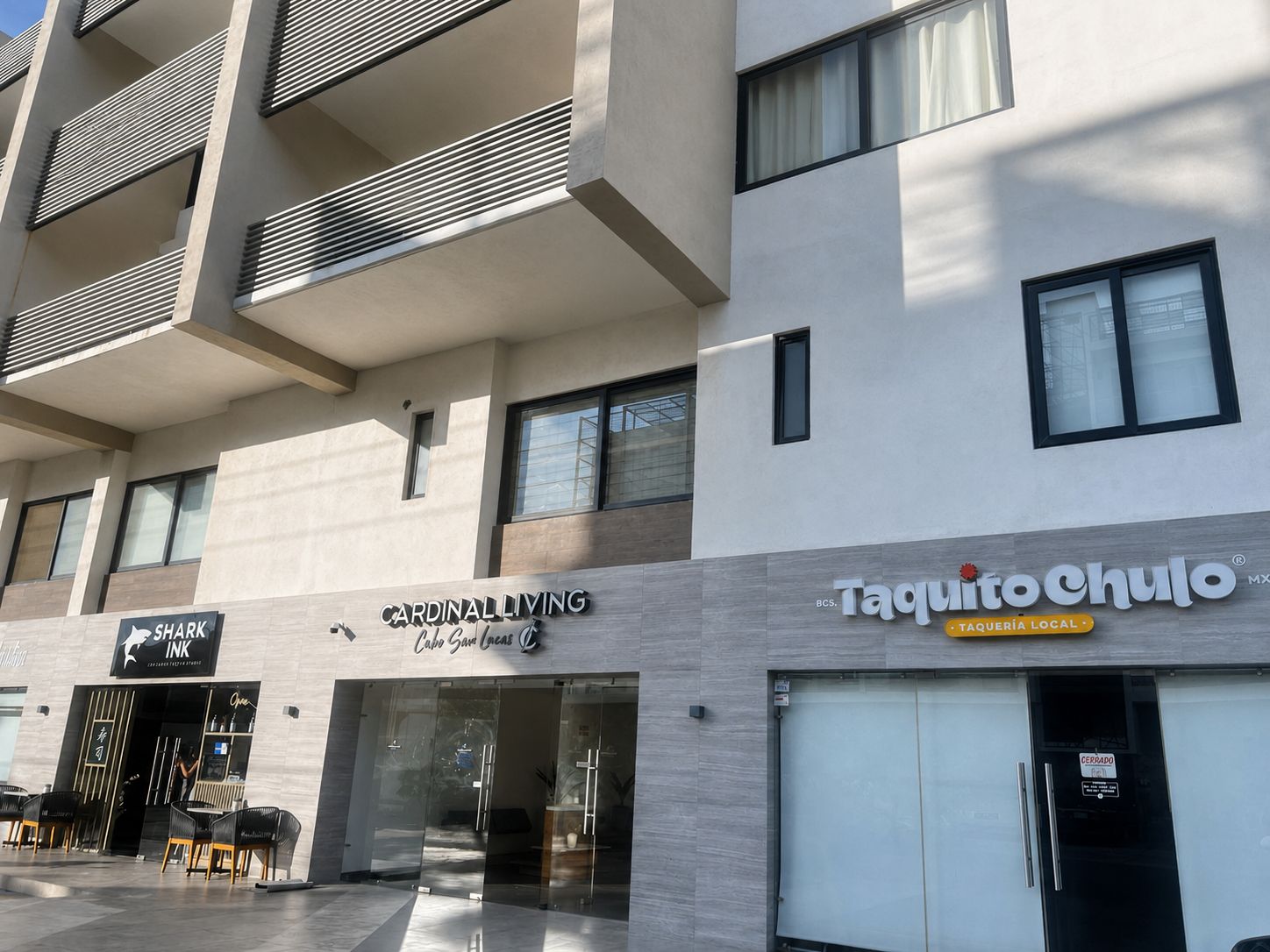 Un immeuble à plusieurs étages dont le rez-de-chaussée est occupé par des commerces, notamment un restaurant et un salon de tatouage.