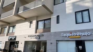 Un immeuble à plusieurs étages dont le rez-de-chaussée est occupé par des commerces, notamment un restaurant et un salon de tatouage.