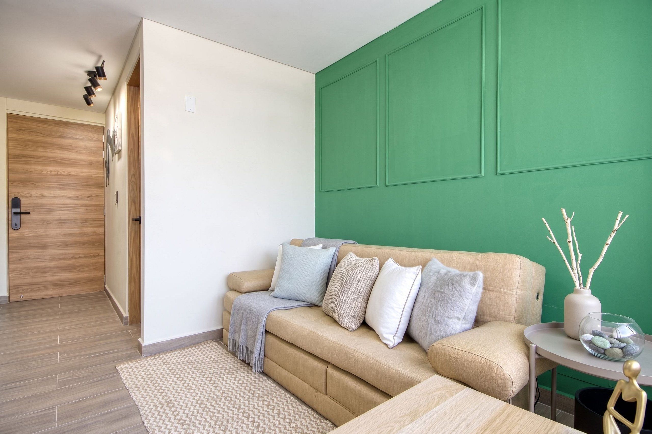 Una sala de estar moderna con un sofá color beige, una mesita redonda y una pared de acento verde.