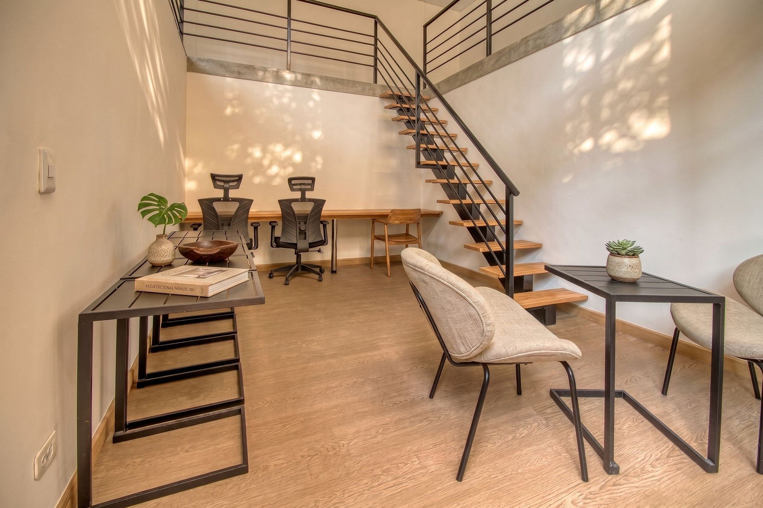 A modern interior with a staircase, wooden flooring, and furniture including a desk, chairs, and a small table.