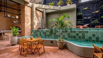 Un área de patio al aire libre con piscina, mobiliario de madera y plantas en macetas.