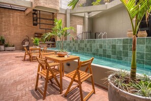Zona de piscina con muebles de madera y plantas en macetas.