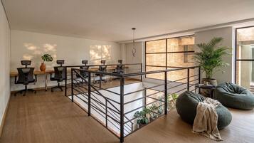 Una habitación amplia con un entrepiso, un comedor con sillas, un ventanal con vistas a un edificio de ladrillo y un sillón de cuero verde.