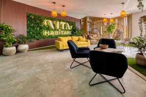 Un salón moderno con un sofá amarillo, sillas negras y una pared verde con el texto 'VITA HABITATRE'.