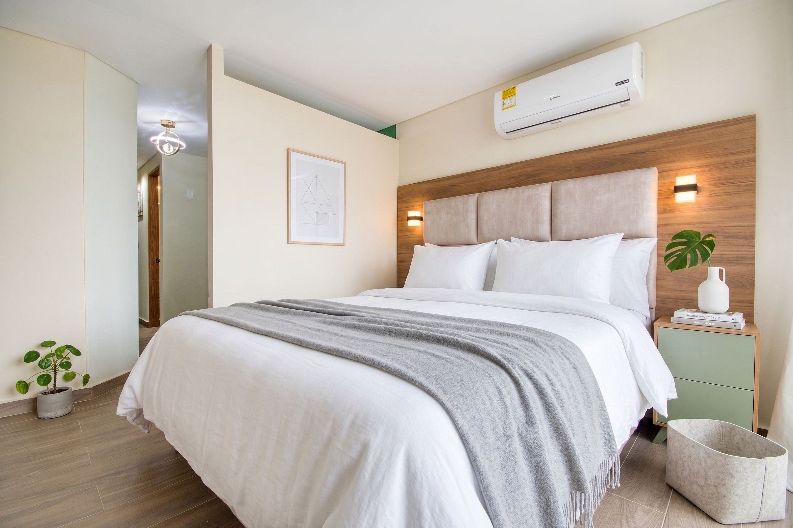 Quarto moderno com cama, mesas de cabeceira, ar condicionado e luminária na parede.