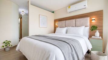 Quarto moderno com cama, mesas de cabeceira, ar condicionado e luminária na parede.