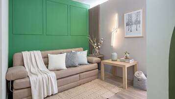Ein modernes Wohnzimmer mit einer grünen Akzentwand, einem beigen Sofa mit Kissen und einem kleinen Holztisch. An der Wand hängt ein gerahmtes Bild.
