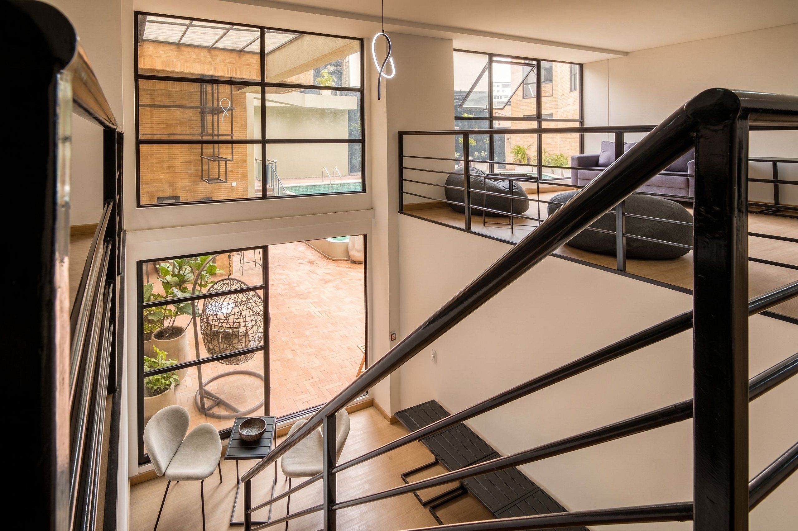 Ein modernes Interieur mit einer Treppe, die zu einem Balkon führt, einer Sitzecke mit Kissen und Blick auf ein Außenbecken.
