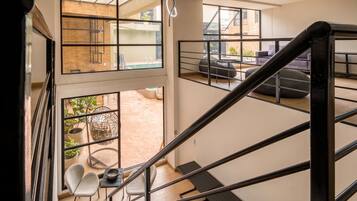 Ein modernes Interieur mit einer Treppe, die zu einem Balkon führt, einer Sitzecke mit Kissen und Blick auf ein Außenbecken.