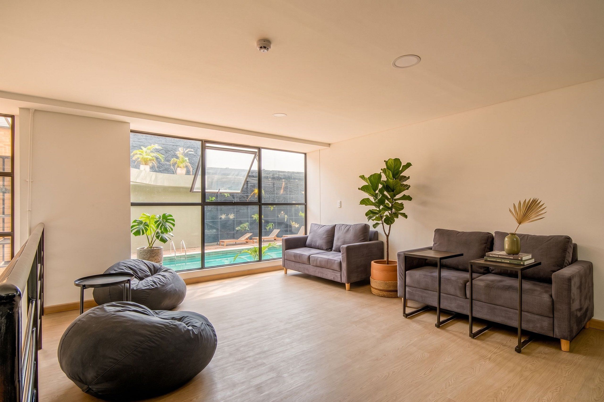 Ein modernes Wohnzimmer mit einem großen Fenster, grauen Sofas, einem Sitzsack und einem kleinen Tisch.