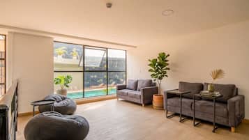 Ein modernes Wohnzimmer mit einem großen Fenster, grauen Sofas, einem Sitzsack und einem kleinen Tisch.
