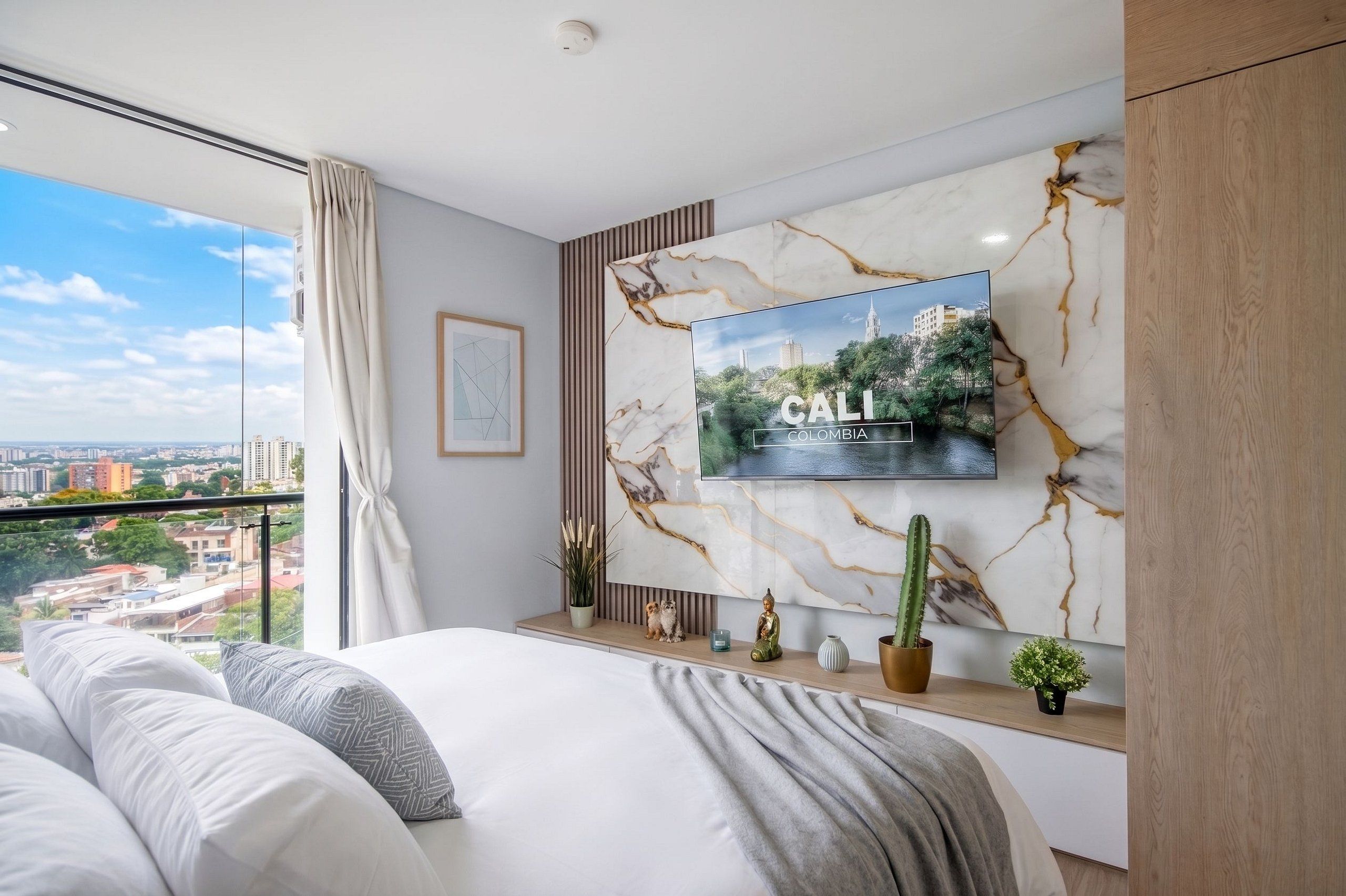 A modern bedroom with a large bed, a mounted TV, and a city view.