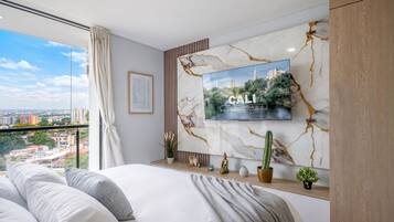 A modern bedroom with a large bed, a mounted TV, and a city view.