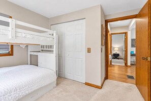 Een slaapkamer met stapelbedden, een kledingkast en een deur naar een andere kamer.