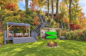A wooden deck with outdoor seating, a fire pit, and a staircase leading to a covered area. - Riverside Retreat | Hot Tub • Sauna • Private Dock (Saugatuck)