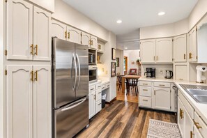 A modern kitchen with white cabinetry, stainless steel appliances, and a wooden floor. - Riverside Retreat | Hot Tub • Sauna • Private Dock (Saugatuck)