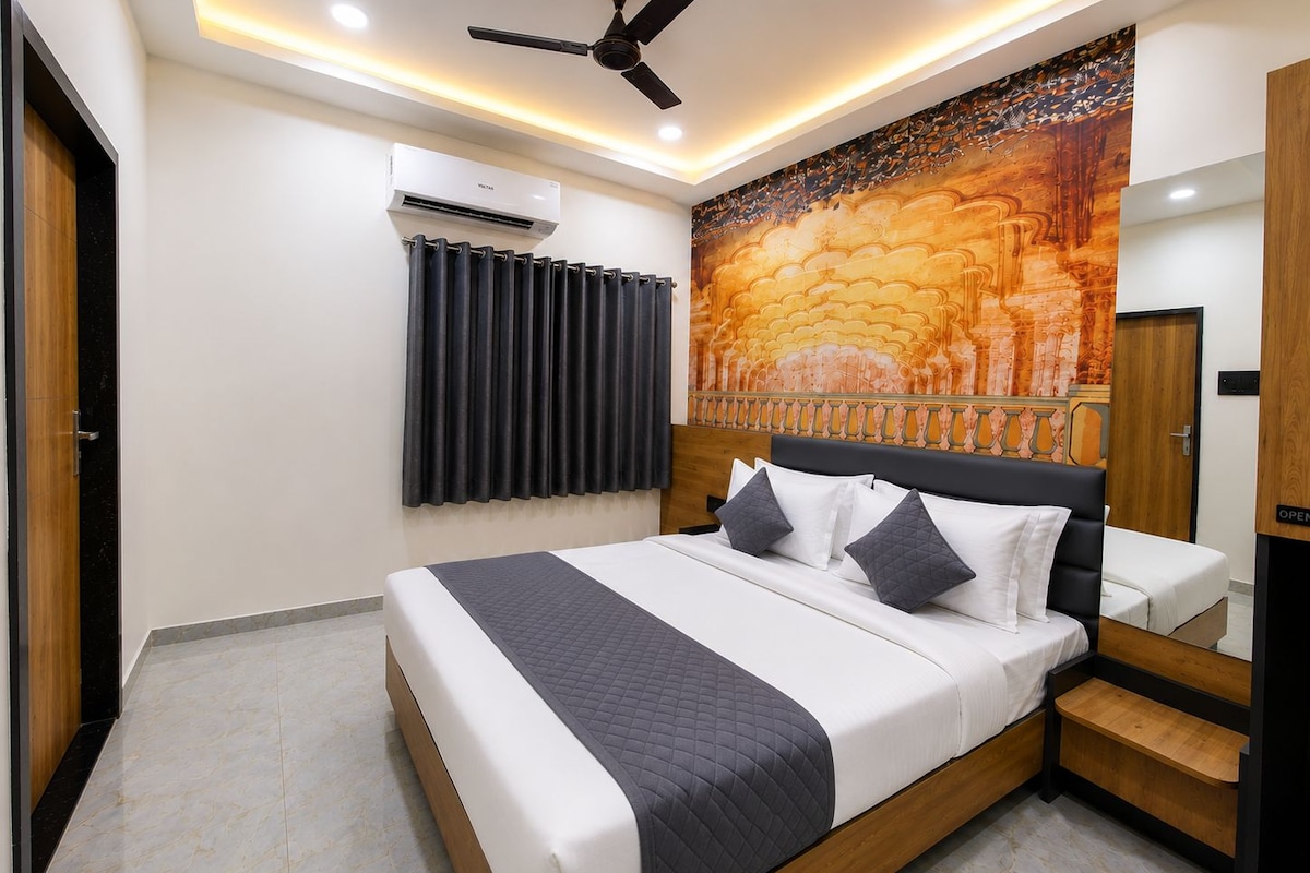 A hotel room with a bed, a ceiling fan, an air conditioning unit, a curtain, and a wall with a mural.