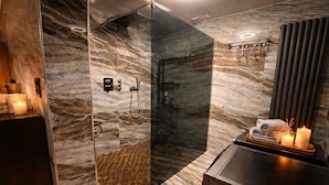 A modern bathroom with a glass-enclosed shower, marble walls, and a vanity with candles.