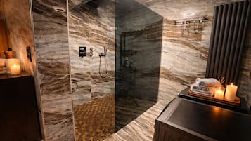 Ein modernes Badezimmer mit einer gläsernen Duschkabine, Marmorwänden und einem Waschtisch mit Kerzen.