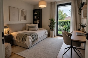 Un dormitorio con cama, mesita de noche, lámpara y vistas al exterior con vegetación.