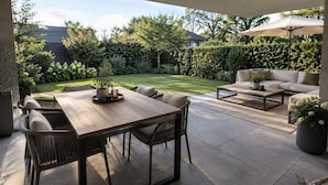 An outdoor patio area with a dining table, chairs, a sofa, and an umbrella.