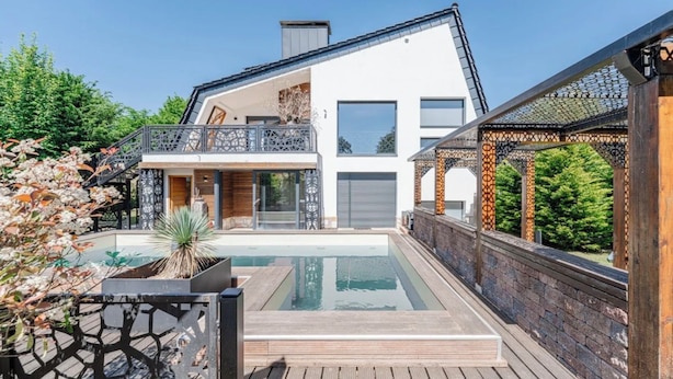 A modern two-story house with a swimming pool, wooden deck, and a covered outdoor area with intricate lattice work.