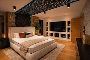A modern bedroom with a large bed, built-in shelving, a flat-screen TV, and a stone accent wall.