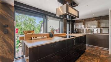 A modern kitchen with a large island, dark cabinetry, and a view of greenery outside.
