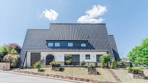 A modern two-story house with a tiled roof, a front entrance with a door, and a small garden area with steps leading up to the entrance.