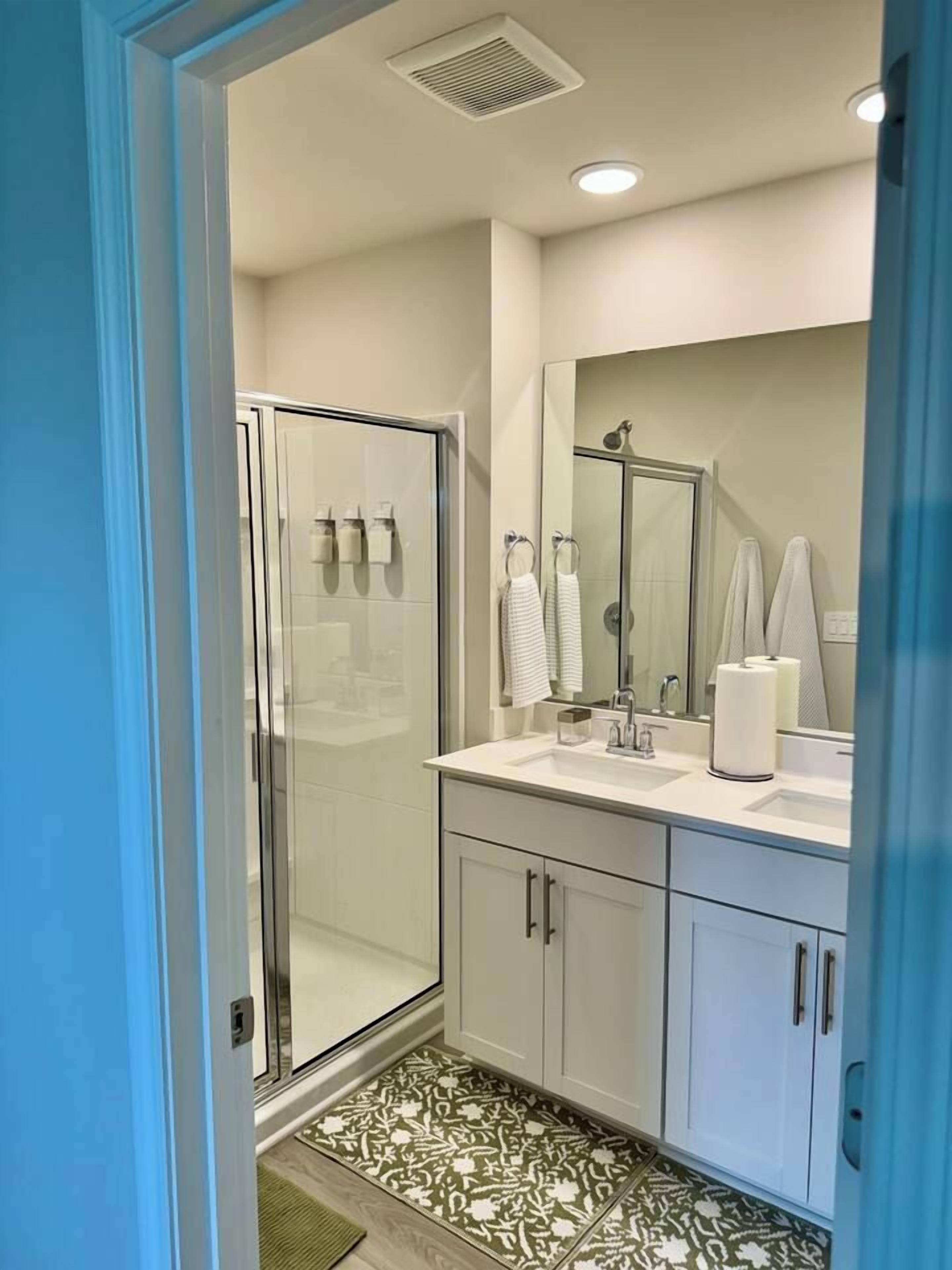 A modern bathroom with a glass shower enclosure, a large mirror, and a white sink.