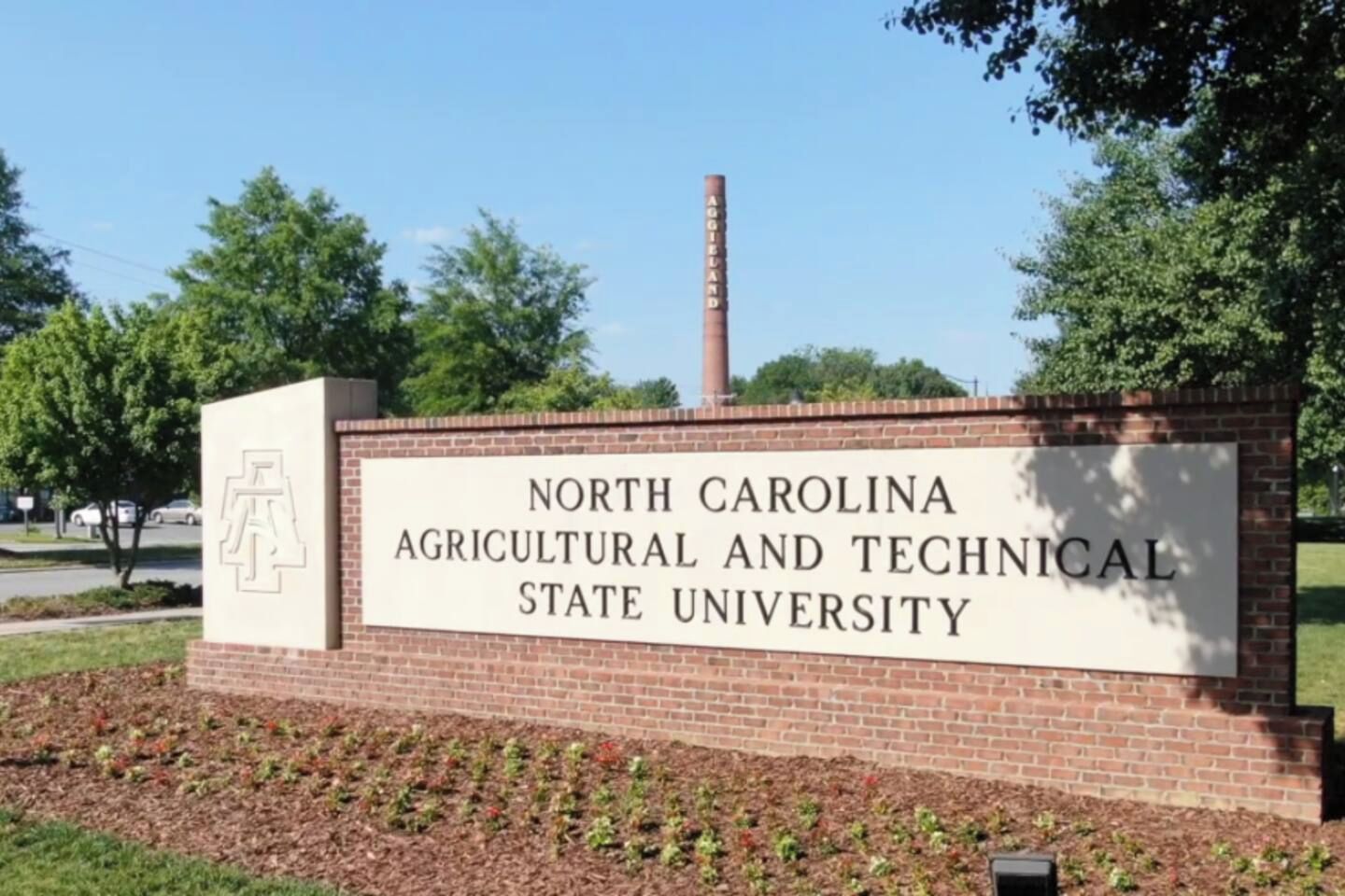 Un cartel de la Universidad Estatal Agrícola y Técnica de Carolina del Norte, con un muro de ladrillo y una chimenea al fondo.