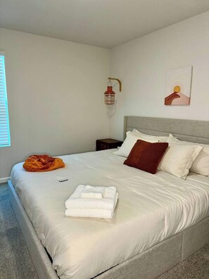 A neatly made bed with white linens, a red throw blanket, and a folded towel on the side.