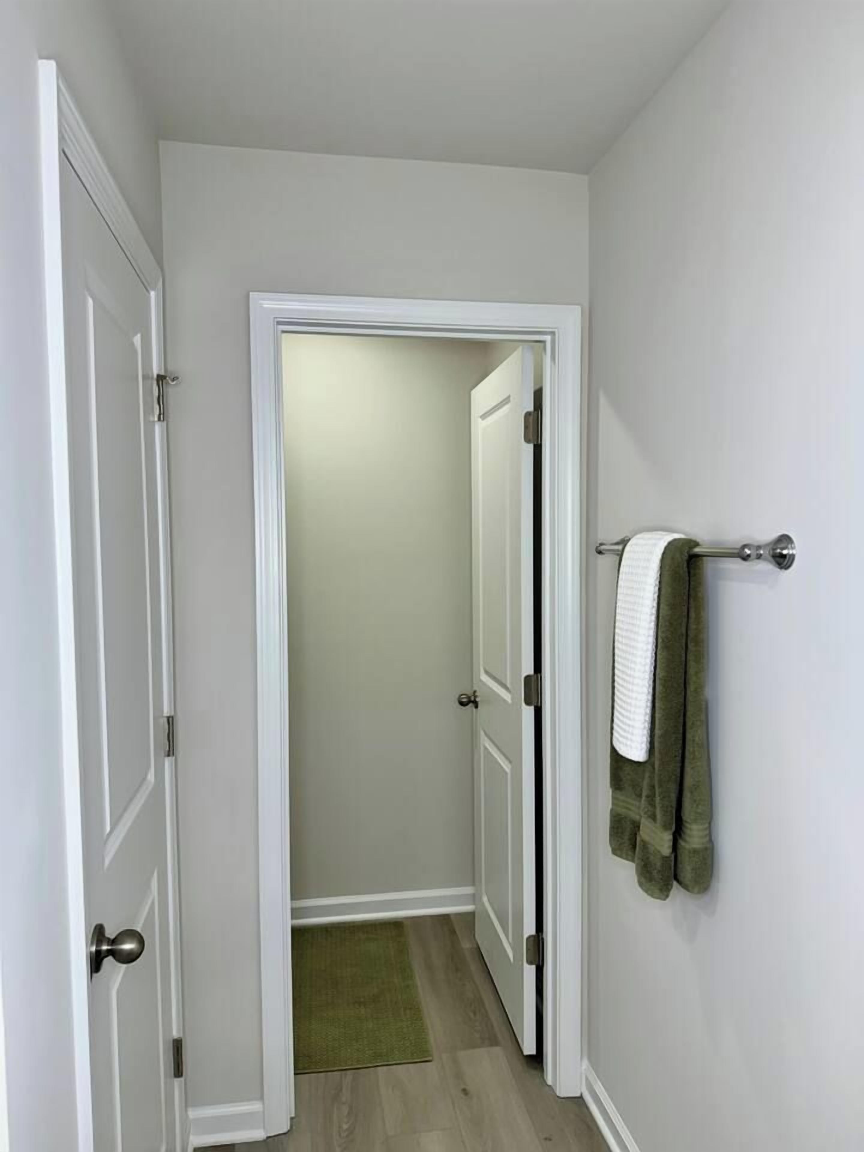 A narrow hallway with white doors, a green mat, and a towel rack with a towel.