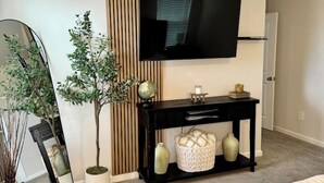 A modern bedroom with a bed, a bedside table, a TV, a mirror, and a potted plant. - Modern Stay w/ 2 King Beds | Near Elon & Downtown (Graham)