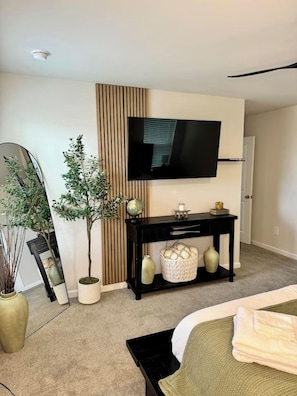 A modern bedroom with a bed, a bedside table, a TV, a mirror, and a potted plant. - Modern Stay w/ 2 King Beds | Near Elon & Downtown (Graham)