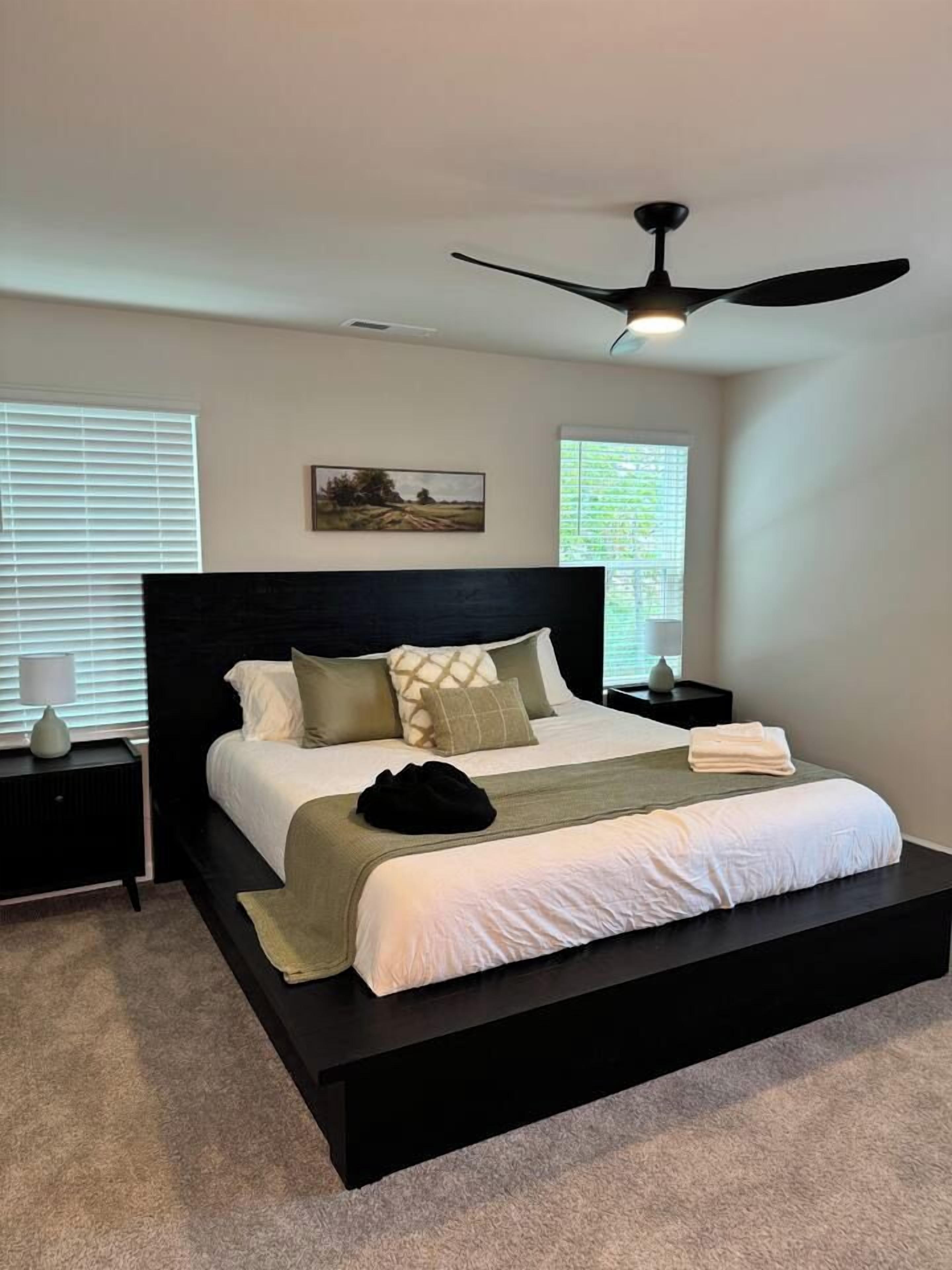 A modern bedroom with a black bed frame, a ceiling fan, and two bedside tables with lamps.