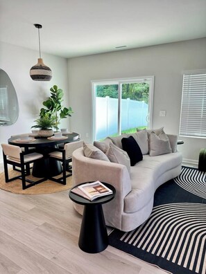 A modern living room with a round dining table, a sofa, a small side table, and a hanging light fixture.