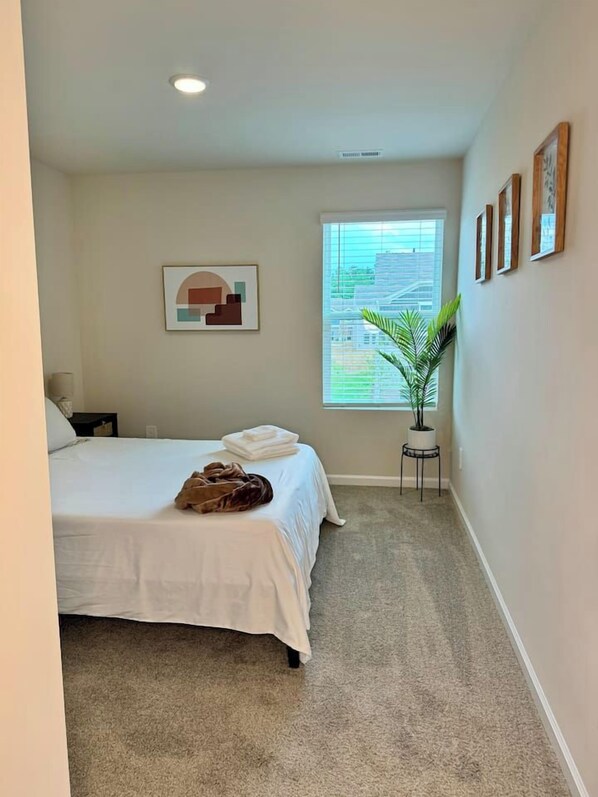 A bedroom with a bed, a window, a plant, and a painting on the wall.