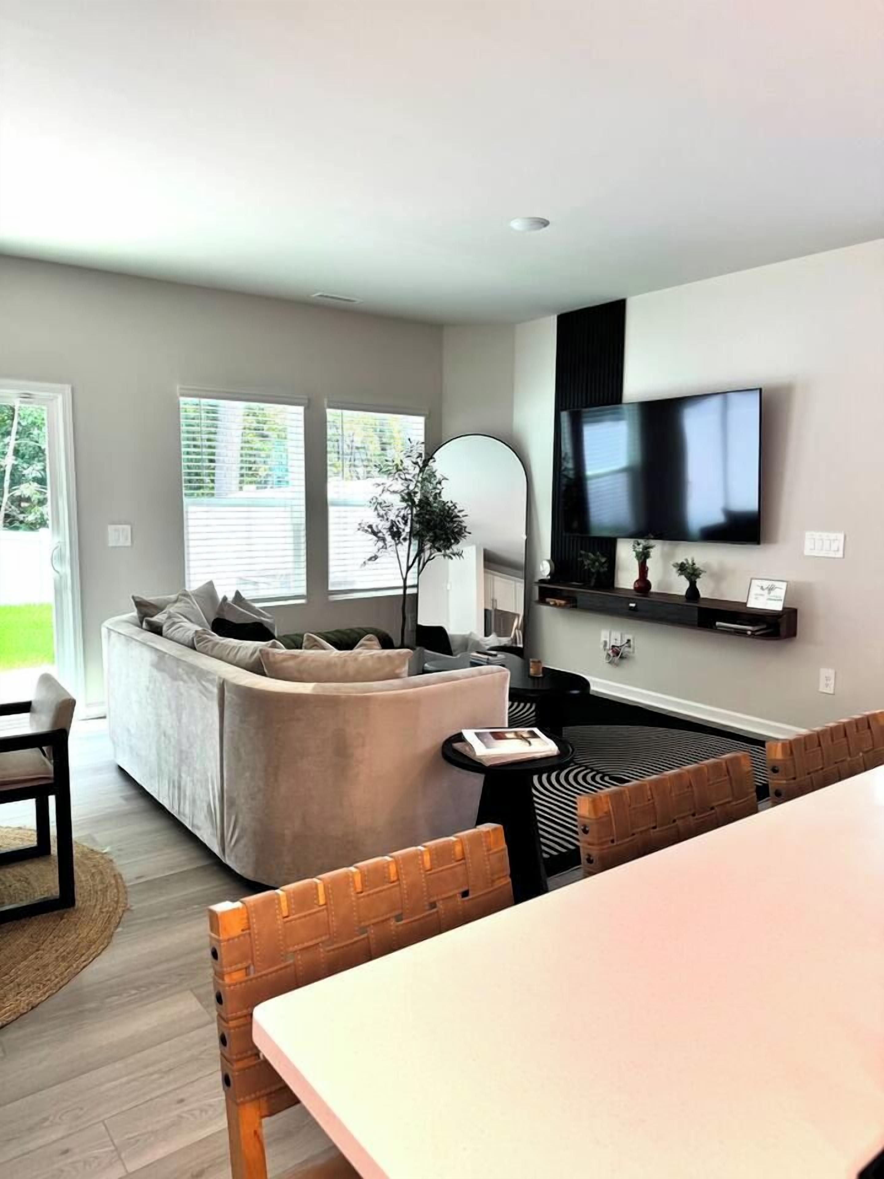 A modern living room with a sofa, a dining table, and a TV mounted on the wall.