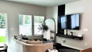 A modern living room with a sofa, a dining table, and a TV mounted on the wall.