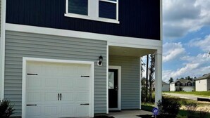 A two-story house with a white garage door, a covered front porch, and a well-maintained lawn. - Modern Stay w/ 2 King Beds | Near Elon & Downtown (Graham)