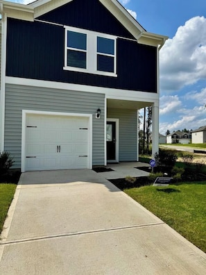 A two-story house with a white garage door, a covered front porch, and a well-maintained lawn. - Modern Stay w/ 2 King Beds | Near Elon & Downtown (Graham)