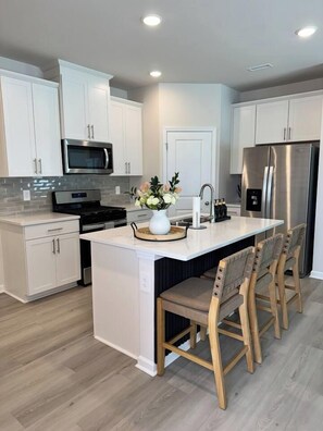 A modern kitchen with white cabinetry, stainless steel appliances, and a central island with seating.