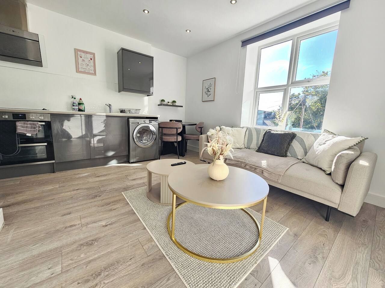 A modern kitchen with built-in appliances, a dining area with a round table, and a sofa with a view of the outdoors.