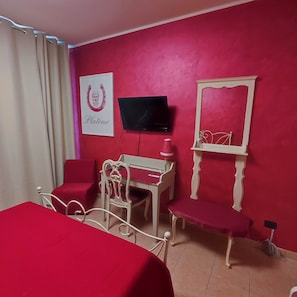 Ein Zimmer mit einem Bett, einem Schreibtisch, einem Sessel, einem Fernseher und einem Spiegel.