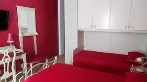 Ein Zimmer mit zwei Betten, einem weißen Schrank, einem Spiegel und einem kleinen Tisch mit einer Lampe.