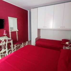 Ein Zimmer mit zwei Betten, einem weißen Schrank, einem Spiegel und einem kleinen Tisch mit einer Lampe.